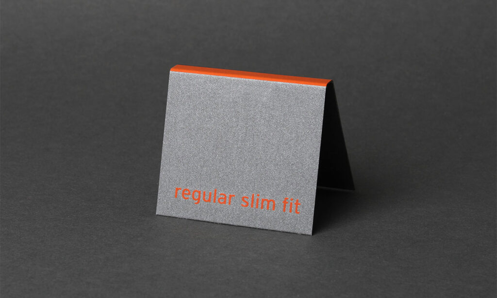 Grauer Bundaufstecker aus hochwertigem Spezialmaterial mit Graphit-Effekt mit orangem „Regular Slim Fit"-Aufdruck und orangefarbenem Kantenstreifen – präzise gestanzte Bundaufstecker für die Modebranche von WEROCA Kartonagen Bielefeld