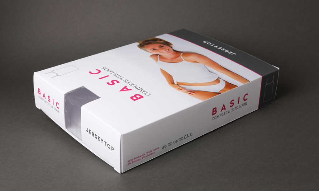 Weiße Faltschachtel mit Fotodruck, pink-schwarzem Aufdruck „Basic – Complete the Look" und transparentem Sichtfenster für ein Jerseytop – individuelle Textilverpackung mit Produktsichtfenster von WEROCA Kartonagen Bielefeld