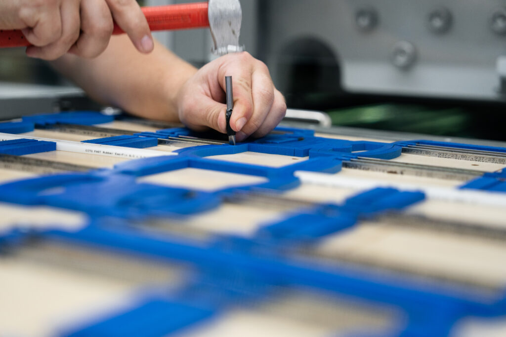 WEROCA employee attaches ejection rubber to a die-cutting form with CITO FAST Rubber EasiFix using a hammer and nail – careful die-cutting form preparation for precise cardboard packaging in Bielefeld