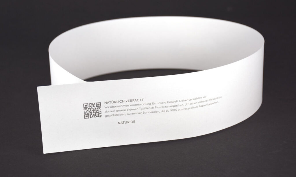 Nachhaltige Fashion-Rundbanderole aus 100% Recyclingpapier mit QR-Code und Nachhaltigkeitsbotschaft für Textilien – WEROCA Kartonagen Bielefeld