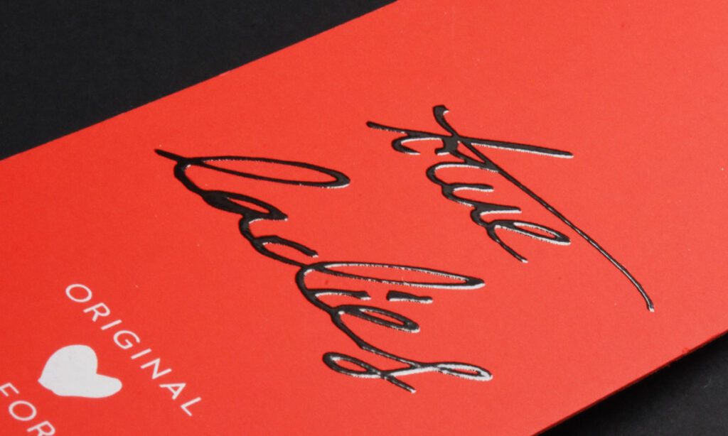 Rotes "True Lovers"-Hangtag von WEROCA Kartonagen Bielefeld mit geprägtem Schriftzug und Herzsymbol, Detailaufnahme für Fashion & Textil-Hangtags.