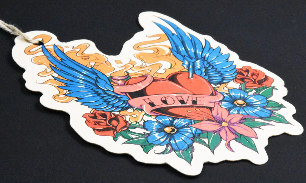 Konturgestanztes "Love"-Hangtag von WEROCA Kartonagen Bielefeld mit geflügeltem Herz-Tattoo-Motiv und bunten Blumen, Detailaufnahme für Fashion & Textil-Hangtags.
