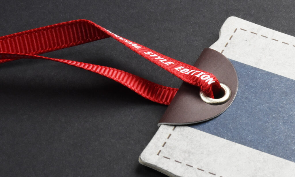 Rotes "Style Edition"-Textilband von WEROCA Kartonagen Bielefeld an einem gestreiften Hangtag mit Lederpatch und Metallöse, Detailaufnahme für Fashion & Textil-Hangtags.