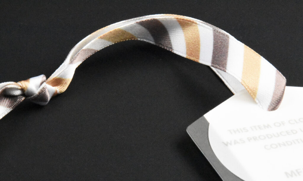 Gestreiftes Satinband von WEROCA Kartonagen Bielefeld an einem weißen Hangtag mit Herstellungshinweis, Detailaufnahme für Fashion & Textil-Hangtags.