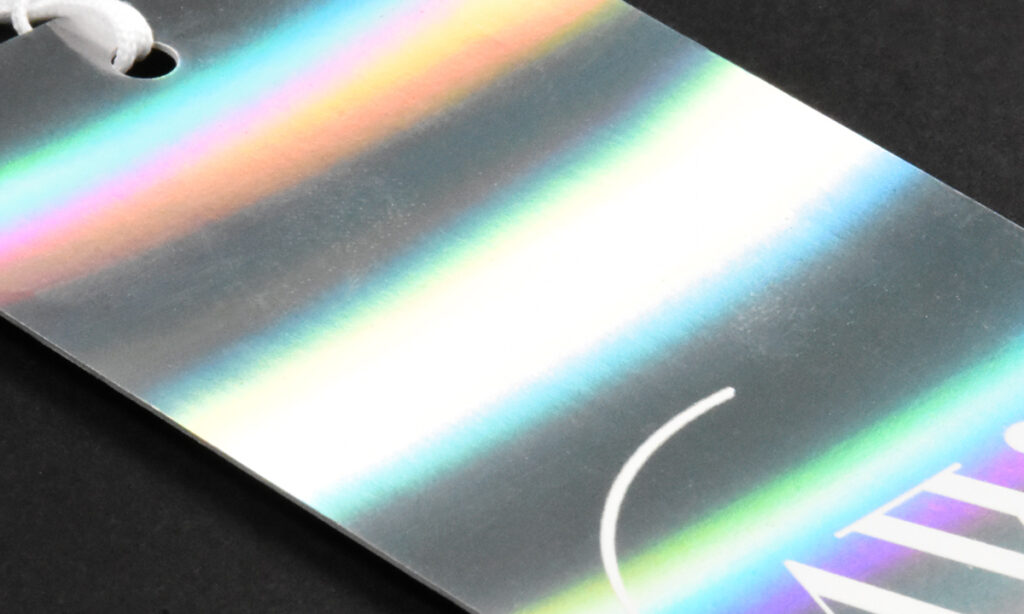 Holografisches Hangtag von WEROCA Kartonagen Bielefeld mit Regenbogen-Reflexionseffekt und weißer Kordel, Detailaufnahme für Fashion & Textil-Hangtags.