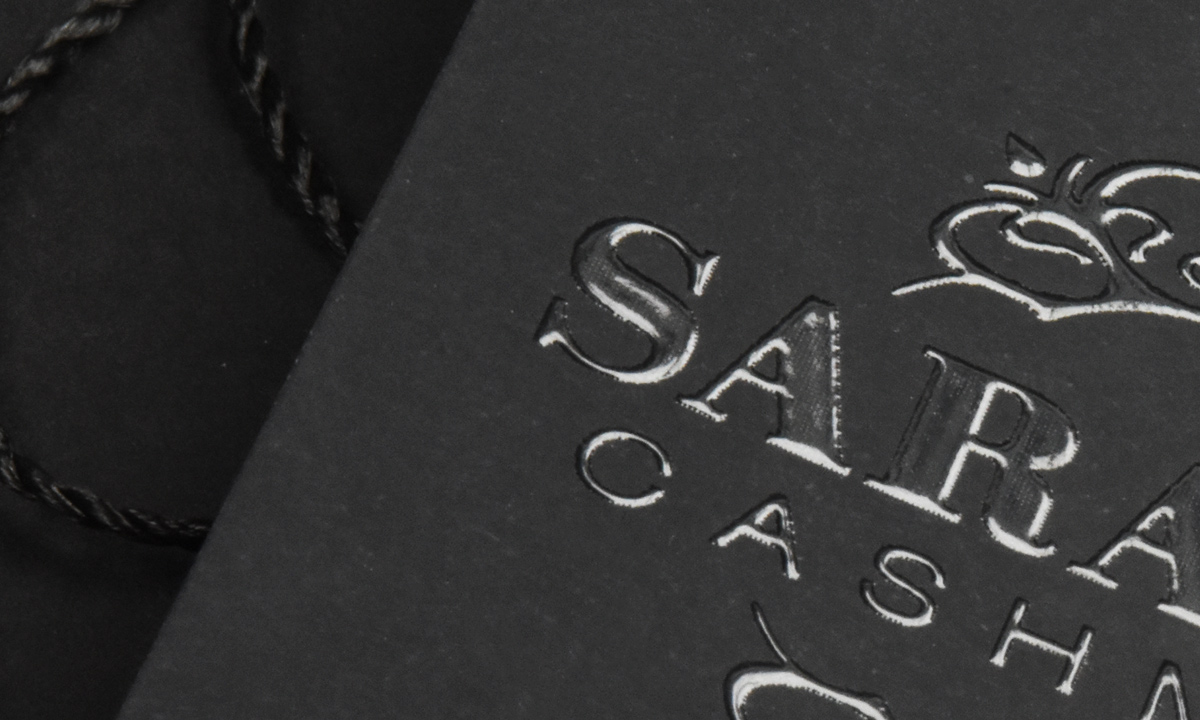 Schwarzes "Sara Cashmere"-Hangtag von WEROCA Kartonagen Bielefeld mit geprägtem Kronenlogo und schwarzer Kordel, Detailaufnahme für Fashion & Textil-Hangtags.